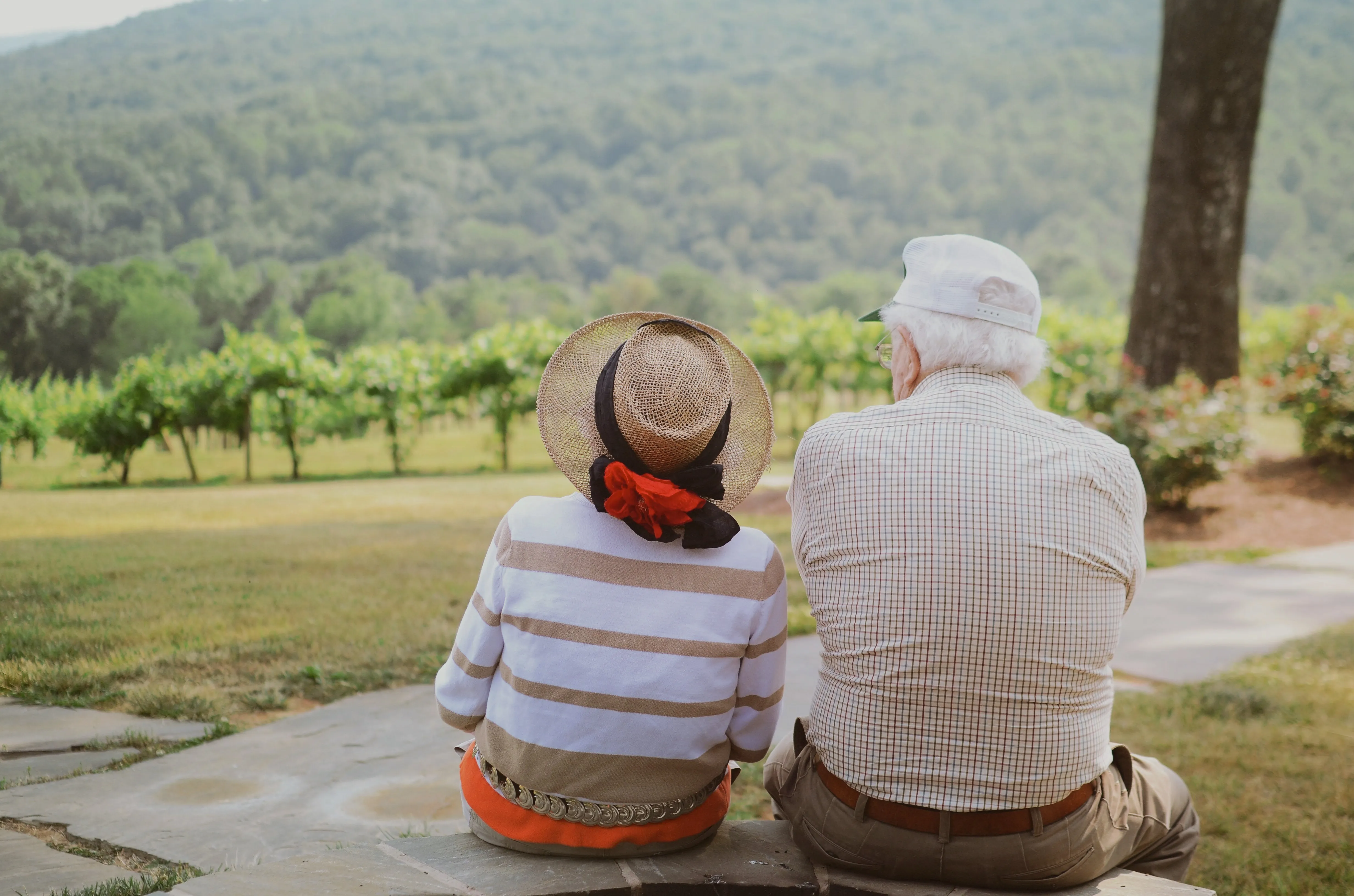 An older couple sitting together in front of a forested hill.